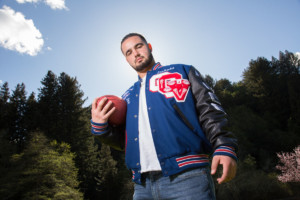 Football player with ball and letterman jacket looks down